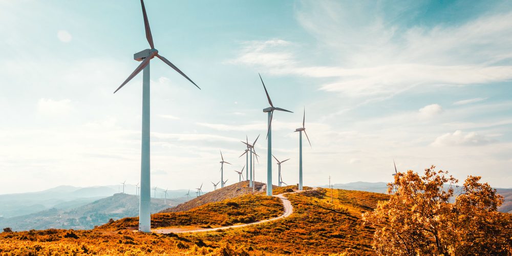 Wind turbines on beautiful sunny summer autumn mountain landsape. Curvy road through mountain Eolic park. Green ecological power energy generation. Wind farm eco field