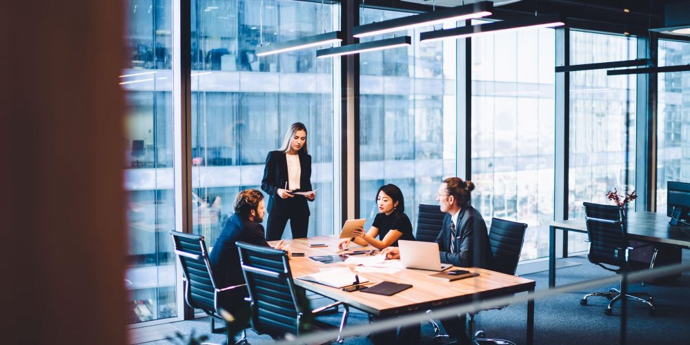 From above of group of diverse colleagues in formal clothing discussing business ideas while gathering at table in modern office and working together
