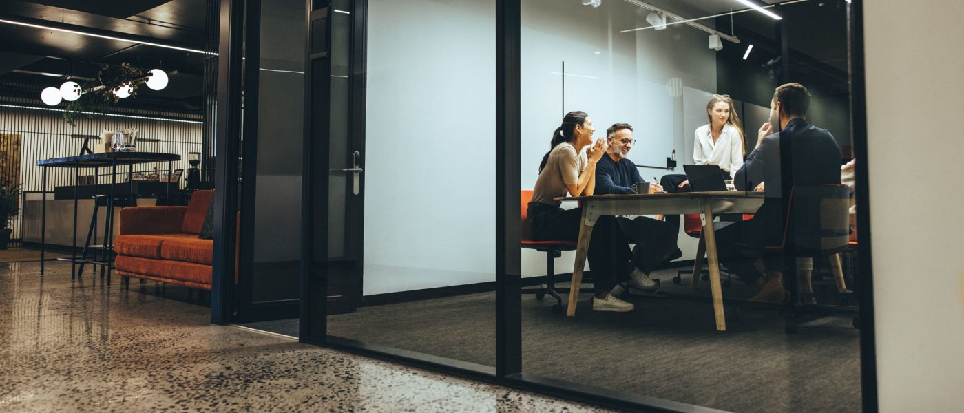 Business colleagues having a meeting in a transparent boardroom. Group of happy business professionals having a discussion during a briefing. Diverse businesspeople collaborating on a new project.